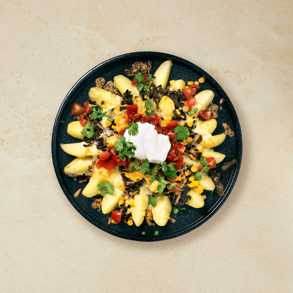 Texmex potetbåter laget i ovnen, med kjøttdeig, salsa, mais, ost og koriander servert på mørk tallerken på beige bakgrunn.