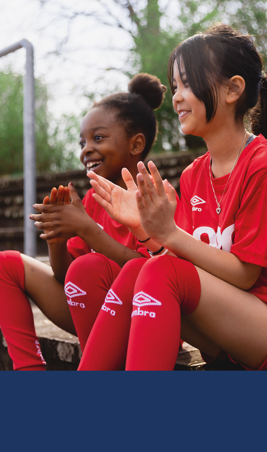 To jenter i røde coop drakter smiler på en benk.