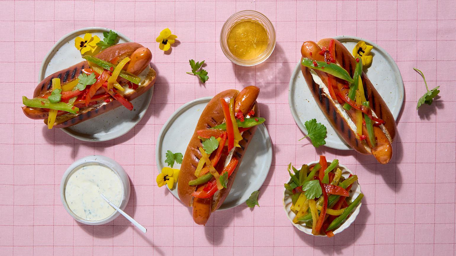Spicy chicken pølse med honninggrillet paprika og hjemmelaget hvitløksdressing servert i grillede pølsebrød på rosa rutete duk.