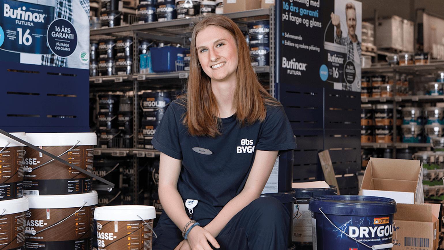 Dame smiler i Obs Bygg butikk foran malingsspann.