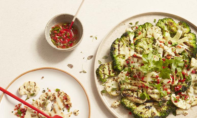 Grillet blomkål og brokkoli med hint av chili, servert på lys tallerken, med en liten skål med dressing av chili og olje ved siden av.