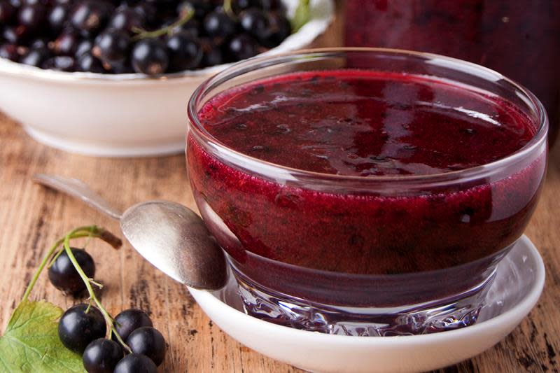 Hjemmelaget solbærsyltetøy i syltetøyskål, med ferske solbær på siden. Rustikk trebakgrunn.