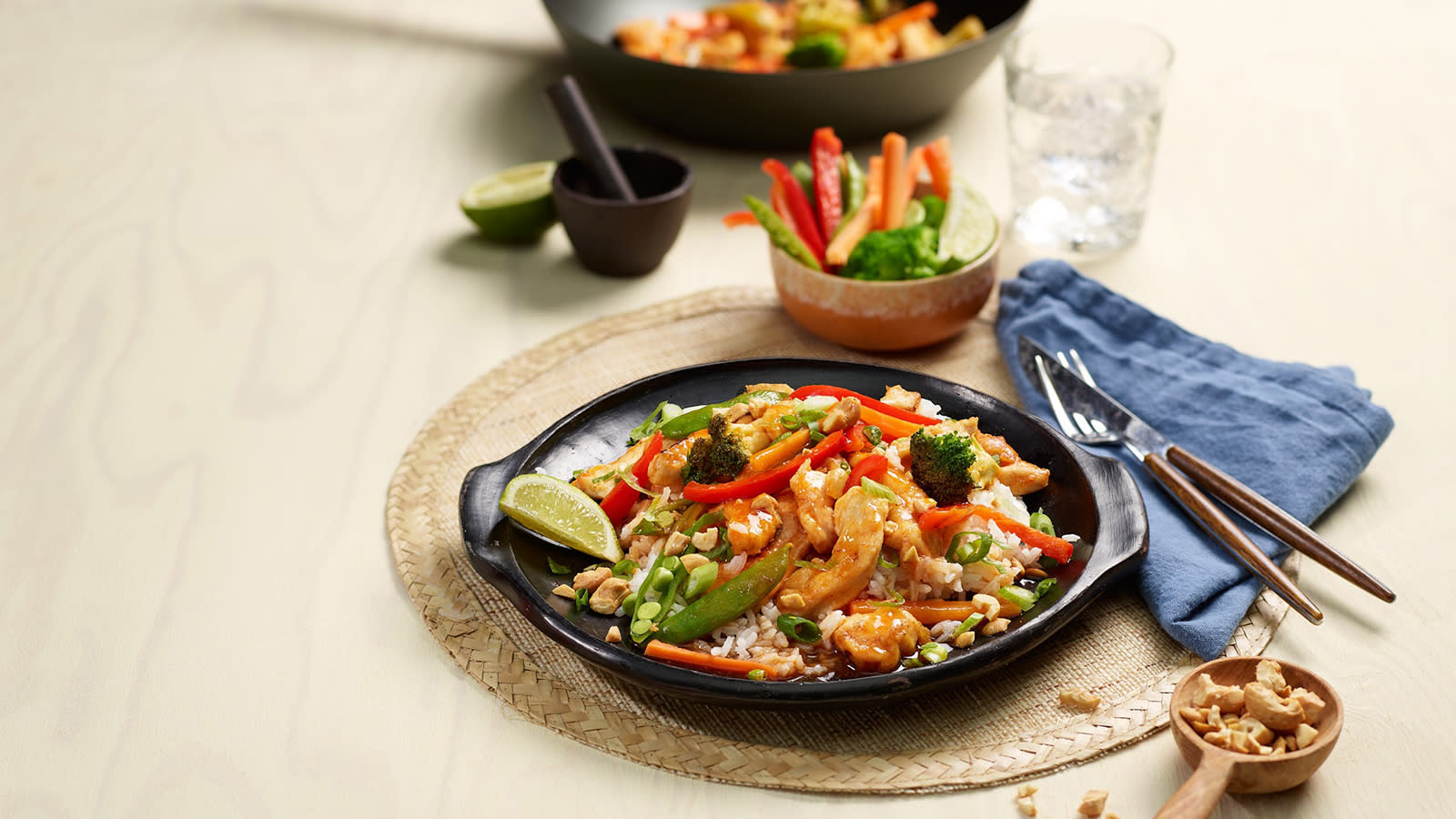 Szechuan wok med crunchy grønnsaker servert i mørk skål på dekket middagsbord. Blå linserviett og vannglass på siden.