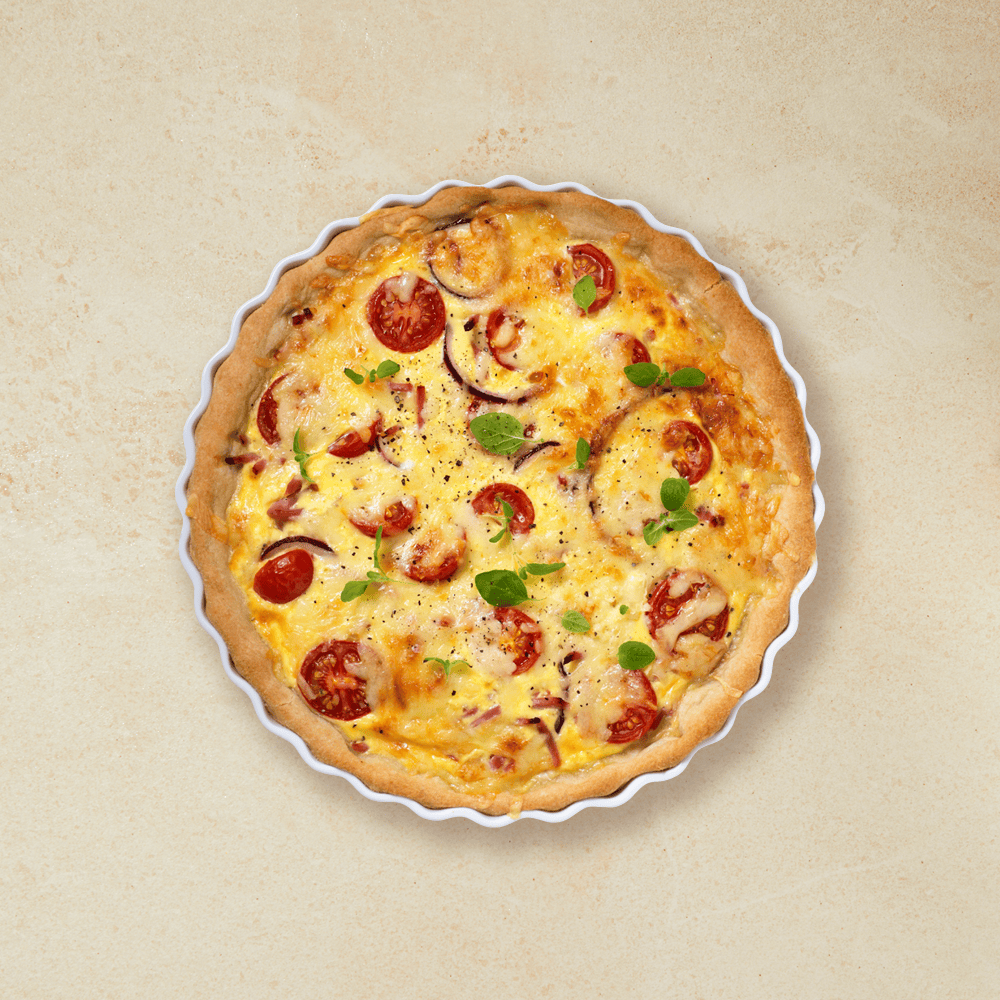 Pai med ost og skinke i en hvit ildfast form, retten er toppet med tomat og løk