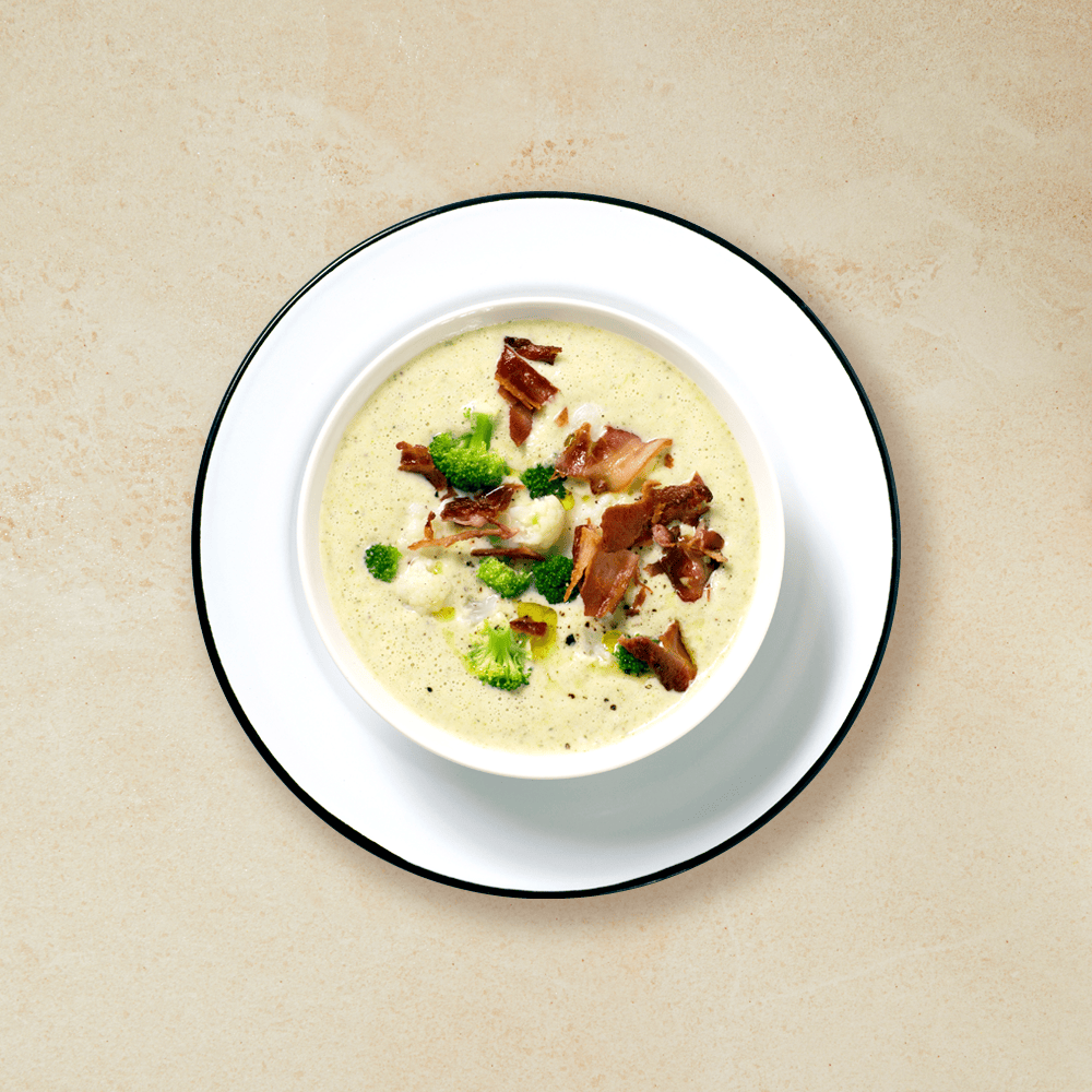 Blomål- og brokkolisuppe med bacon i en hvit skål på en hvit tallerken