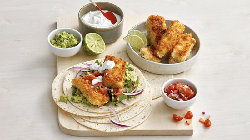 Knasende sprø fisketaco. Tacolefser med panert hvit fisk, tomatsalsa og guacamole på lys trefjøl og lys bakgrunn. 