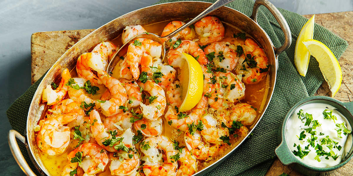 Smørstekte scampi med sitron og persille, servert i ildfast form med ferske urter og sitronbåt. Hjemmelaget saus i liten skål ved siden av.