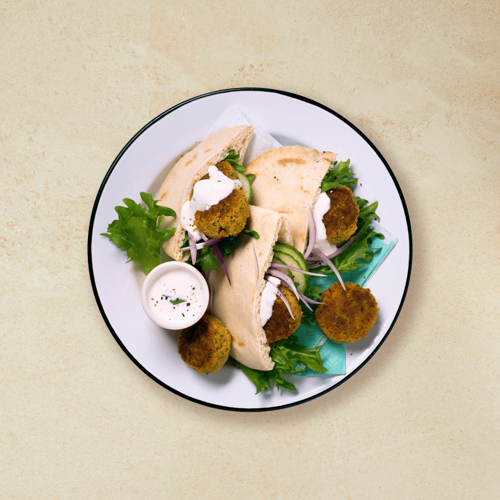 Falafel i pita med grønnsaker og hvitløksdressing på en hvit tallerken