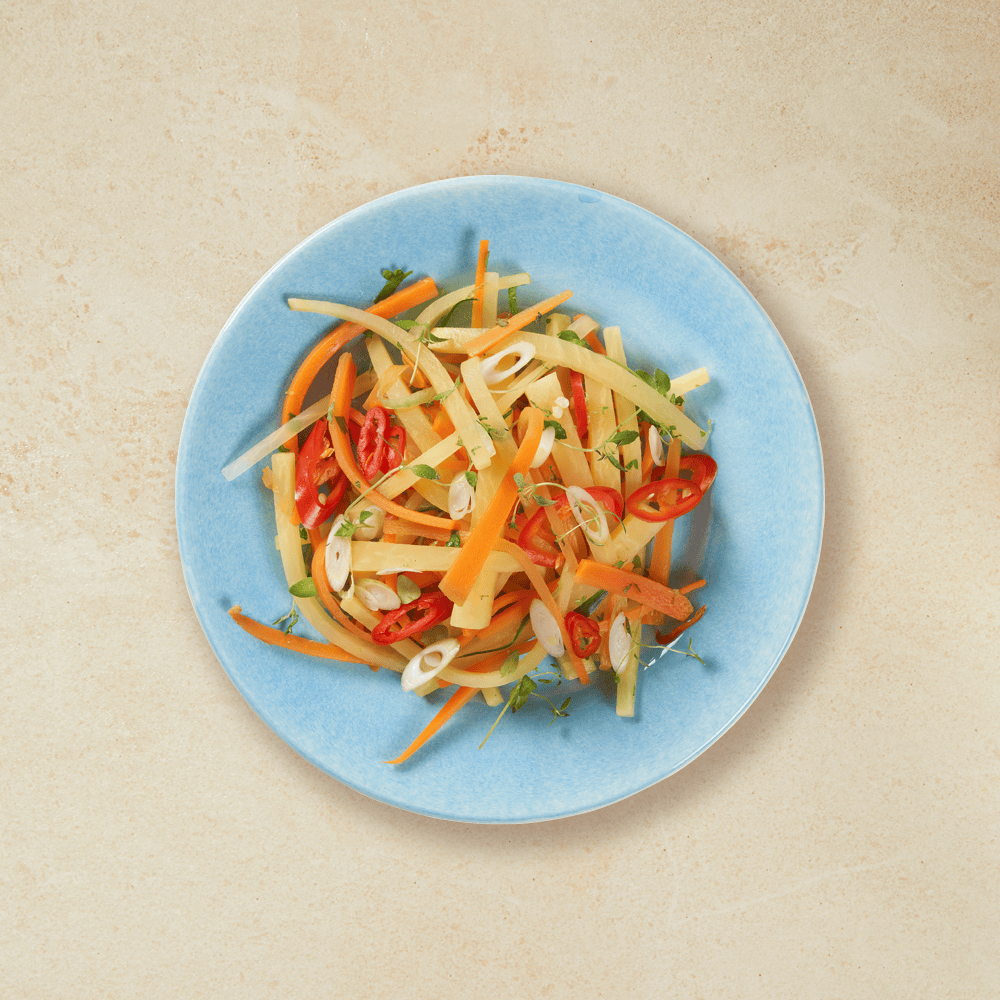 Honningstekt kålrabi og gulrot i strimler, med chili og ingefær servert på lyseblå tallerken.