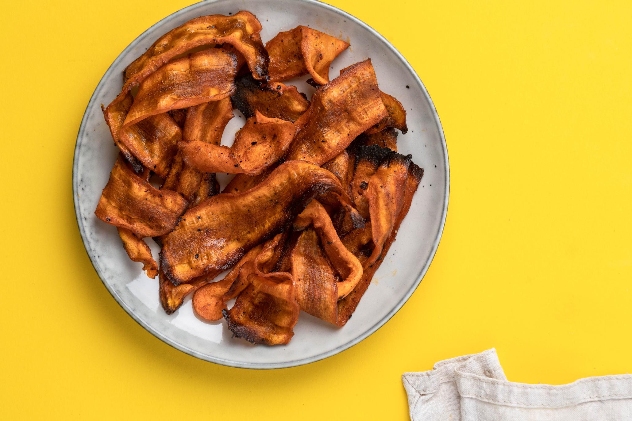 Vegansk gulrotbacon servert på lys tallerken. Gul bakgrunn.