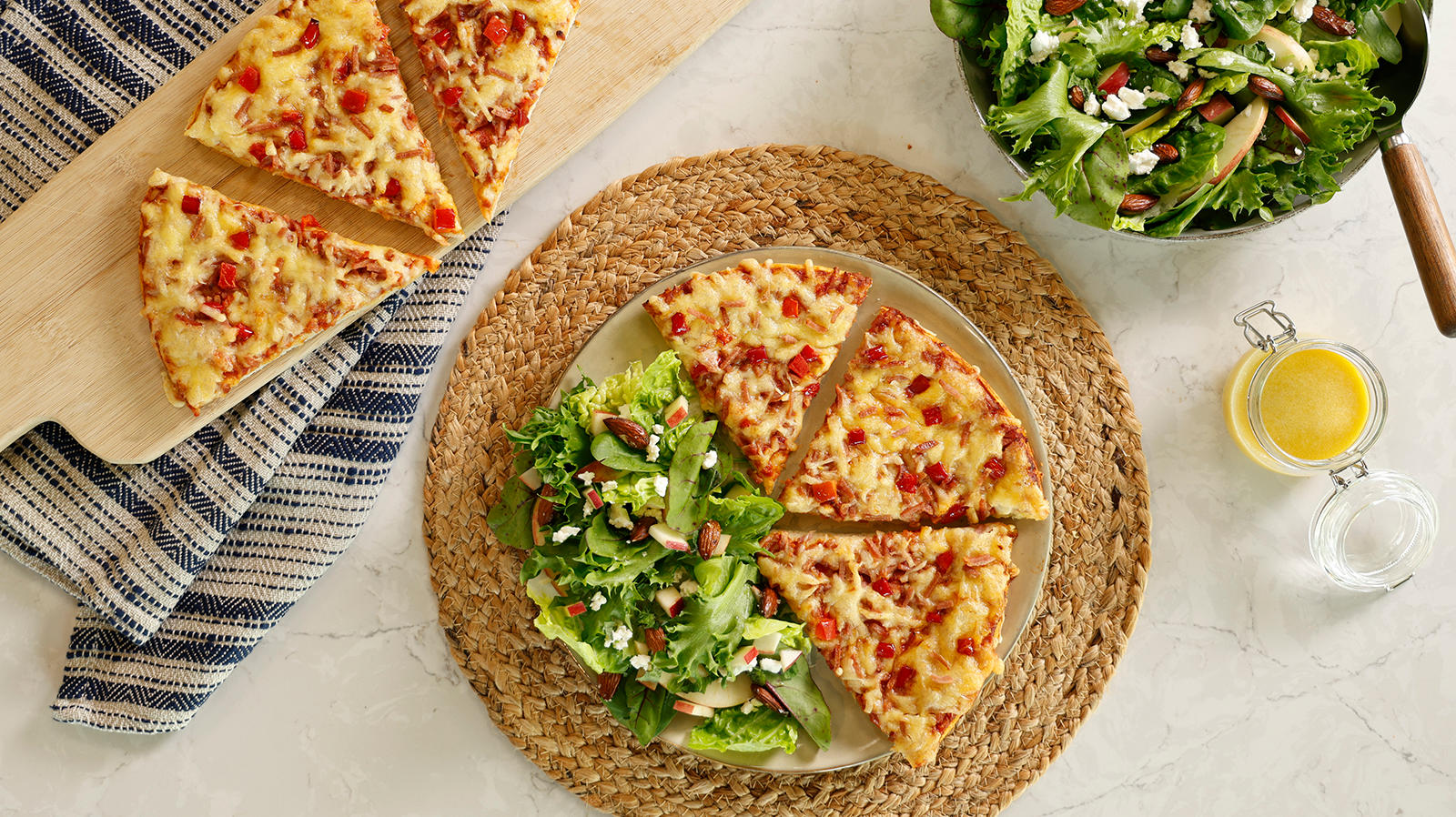 Frisk salat til pizza Grandiosa servert på lys tallerken med tre stykker pizza. Skål med salat, og krukke med dressing ved siden av.