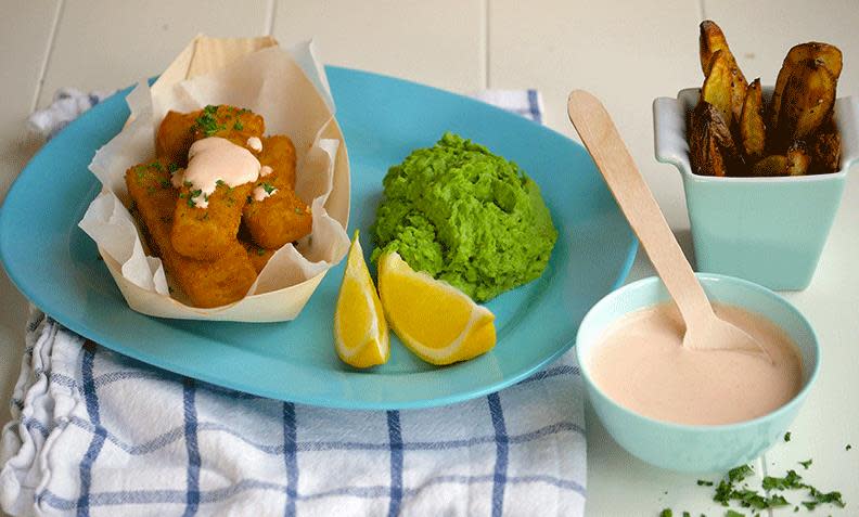 Fiskepinner med ertepuré på turkis middagstallerken. Skåler med stekte potetbåter og dip ved siden av. 