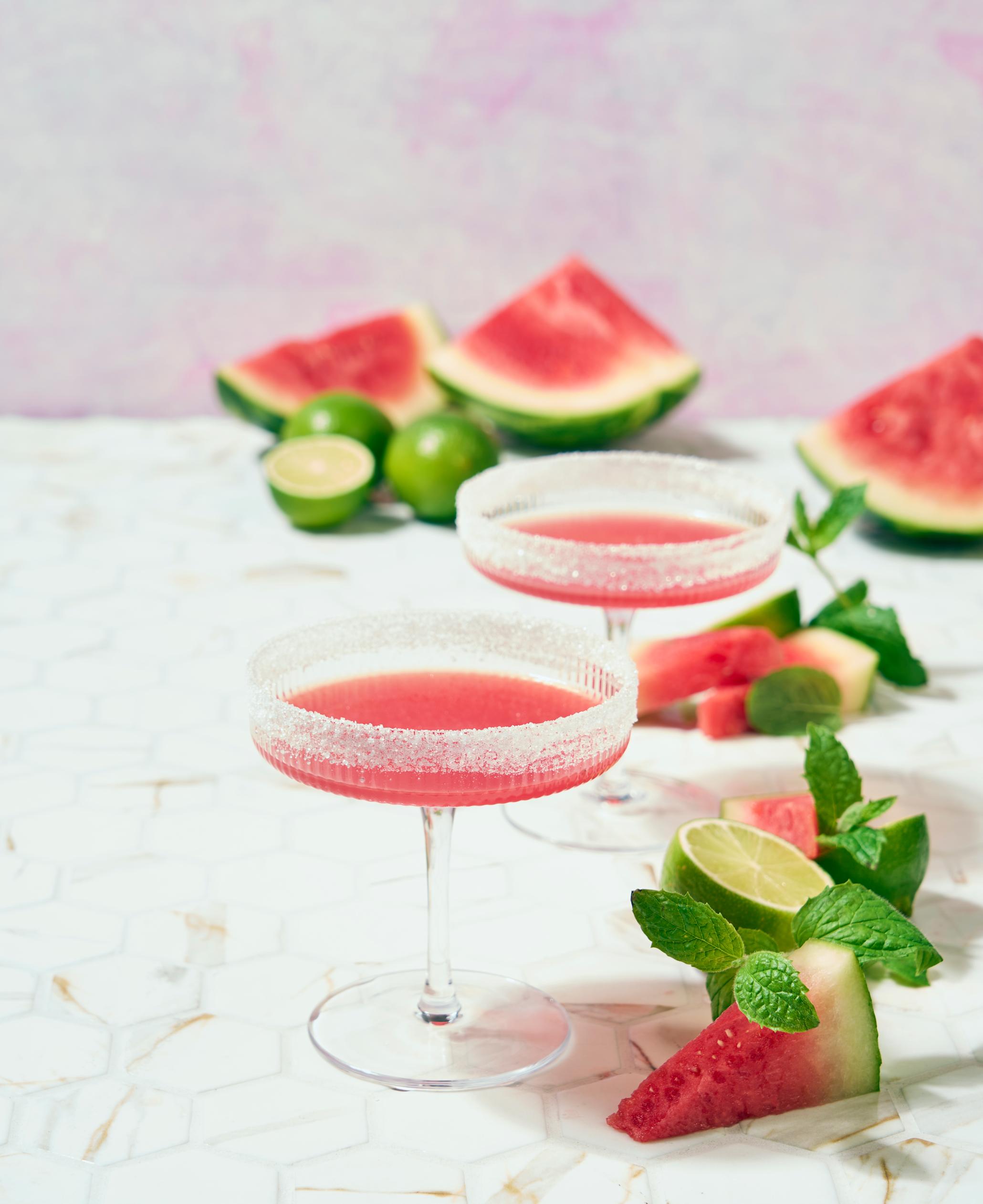 Knall rosa vannmelon margarita - mocktail servert i cavaskåler med sukker på kanten, omringet av vannmelonbiter, frisk mynte og lime.