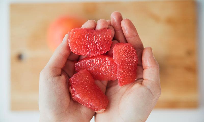 To hender holder fire fileter av grapefrukt over et skjærebrett.