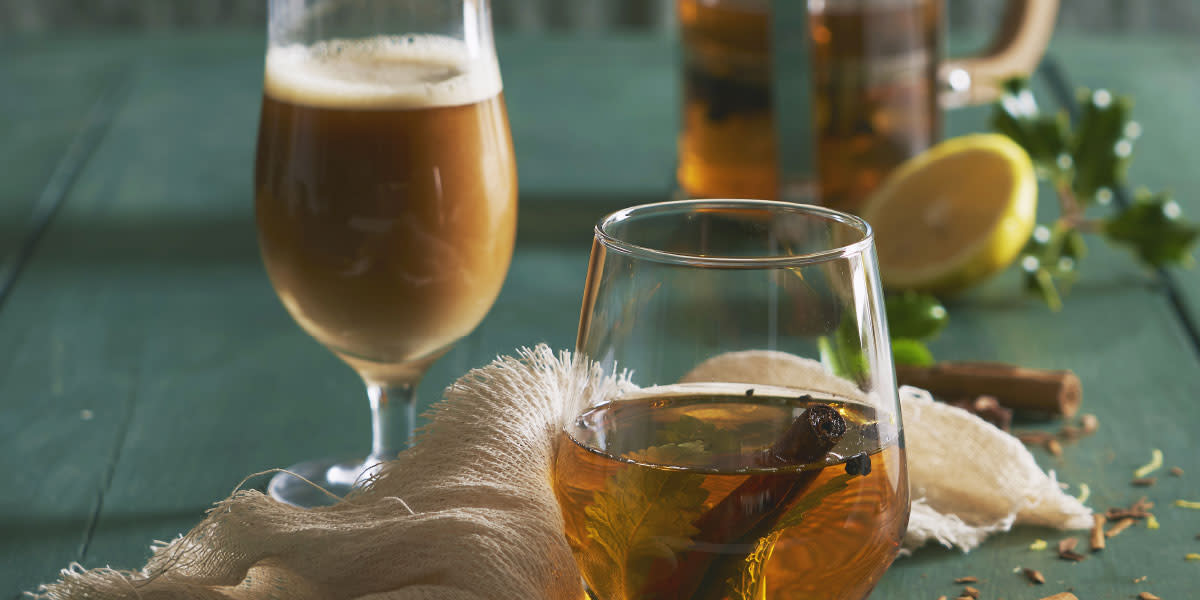 Mulled øl og cider i ølglass på grønt trebord med tørkede krydder og urter.