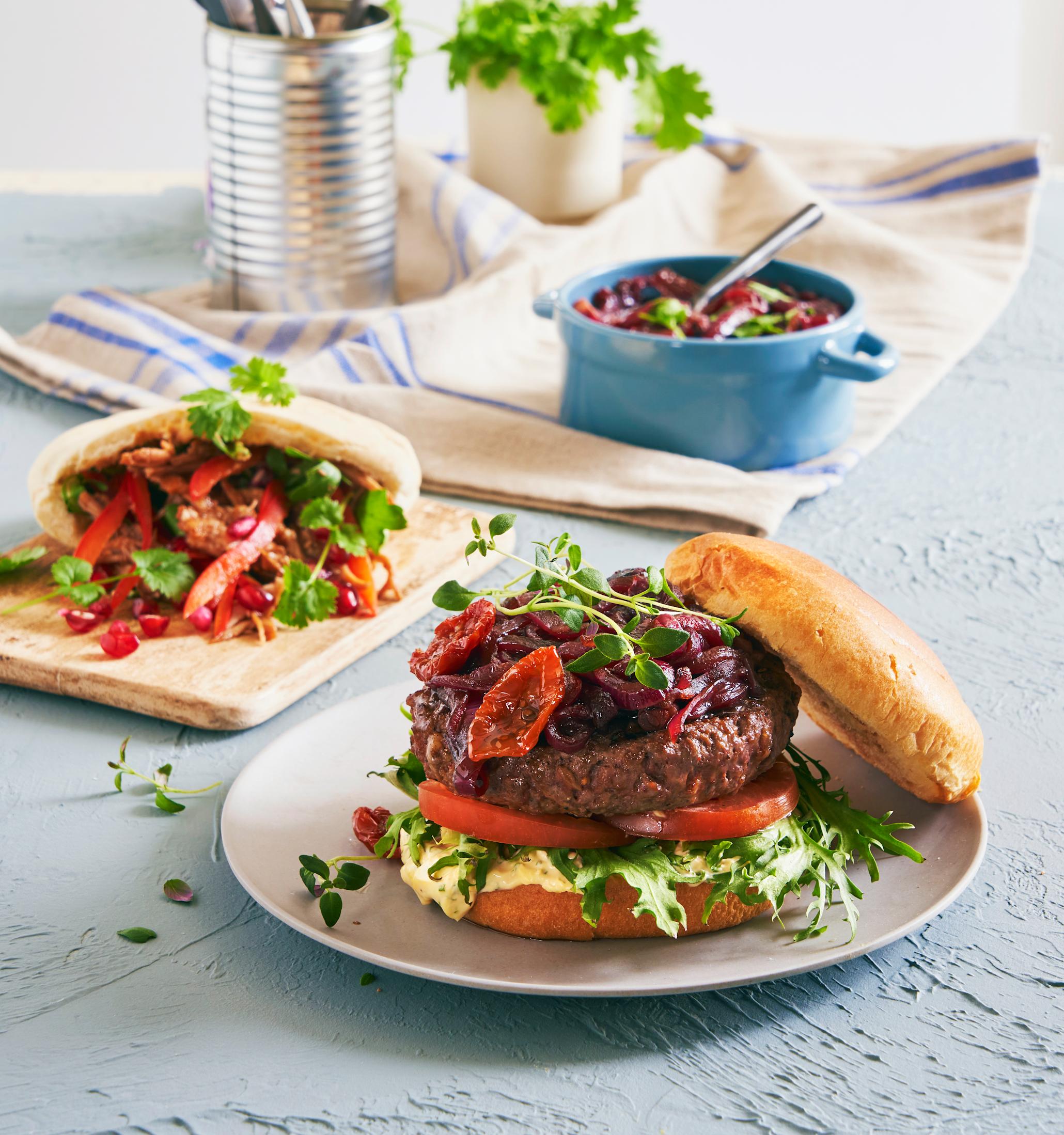 Grov burger med manchegodressing og rødløkmarmelade, på hvit tallerken.