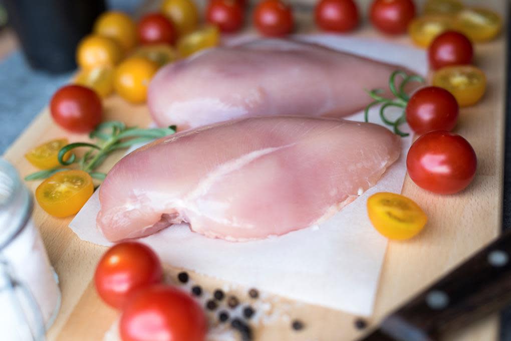 To rå kyllingfileter ligger på kjøkkenpapir på en skjærefjøl, omringet av fargerike cherrytomater.