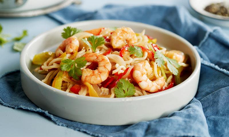 Wok med scampi, nudler, paprika og koriander servert i lys grå bolle på middagsbord med blå linserviett.