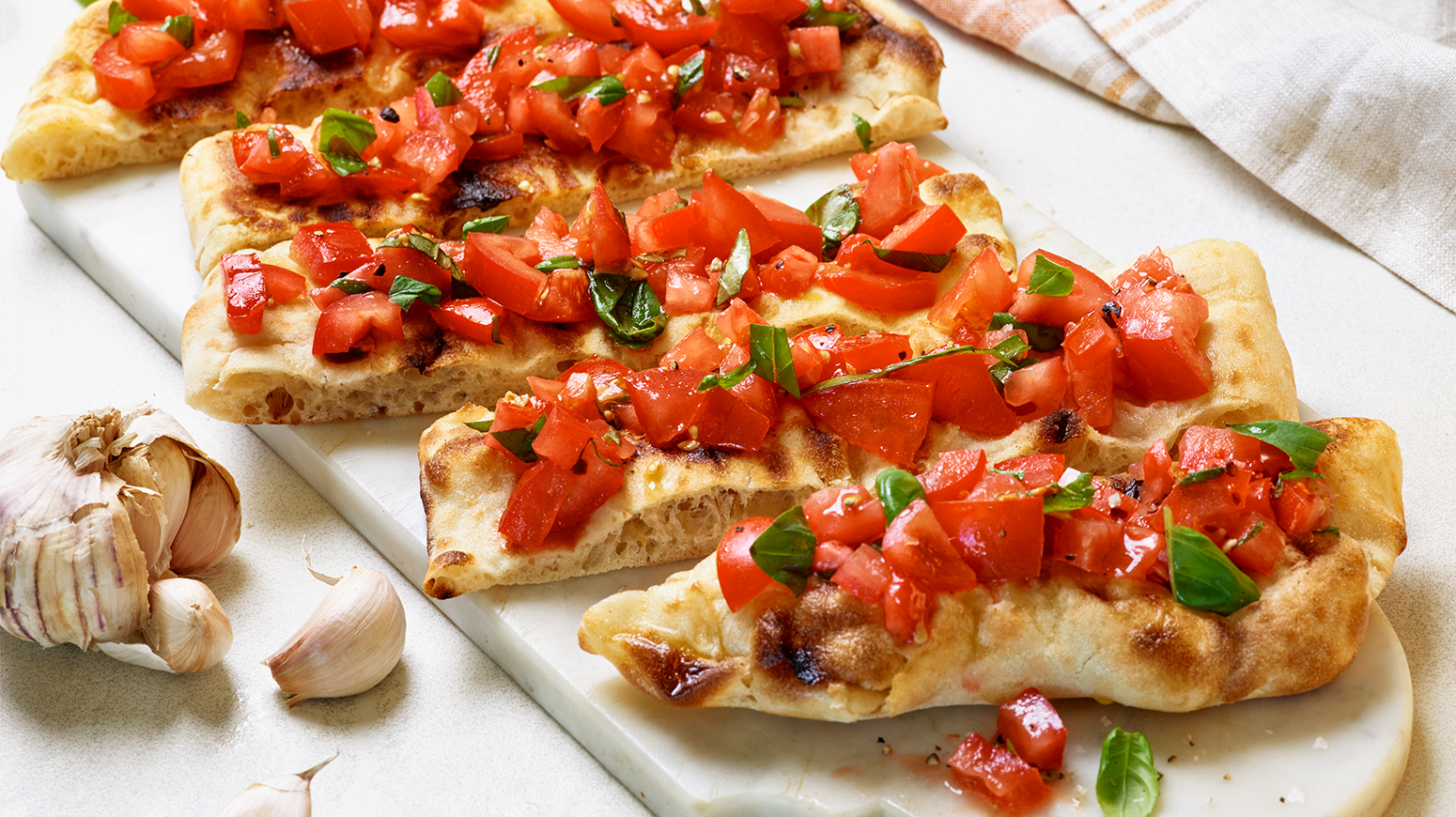 Fire skiver bruschetta med hakkede tomater, basilikum og hvitløk på et hvitt marmorfat.
