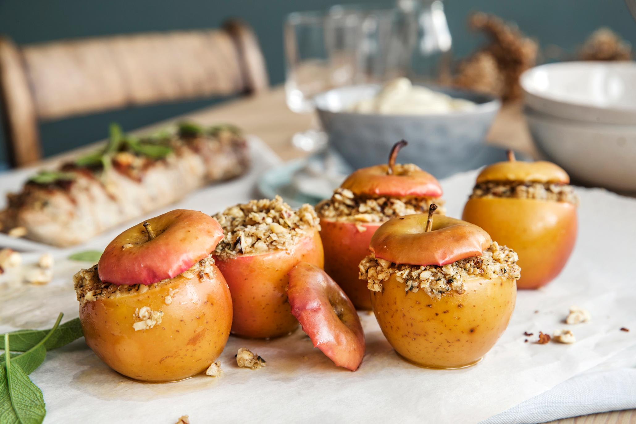 Ovnsbakte epler med urtesmør. Toppen av eplene er skåret av, og eplene er fylt med nøttefyll før toppen er satt på igjen.