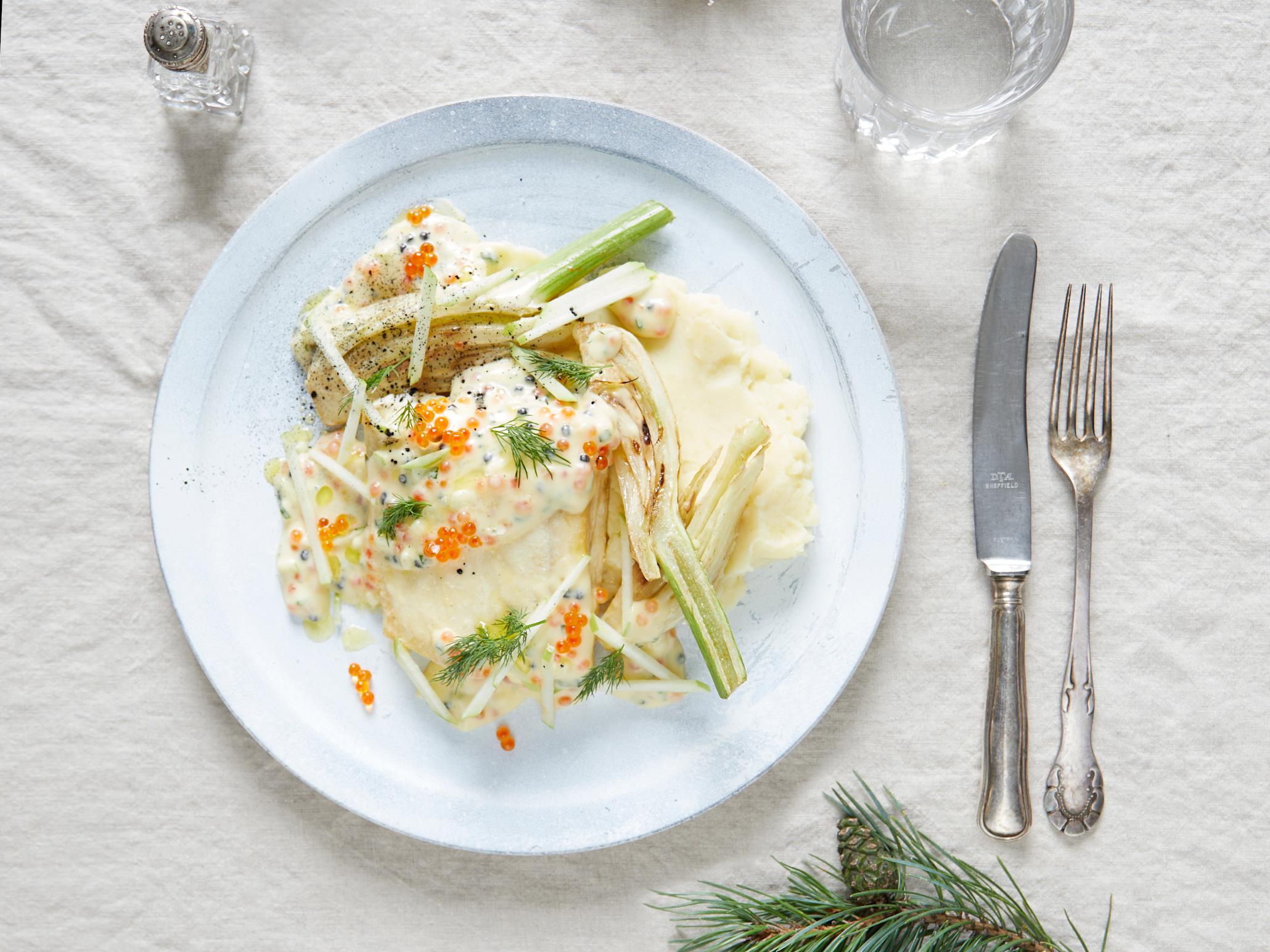 Julekrydret kveite med mandelpotetstappe og smørsaus servert på hvit tallerken på lyst julepyntet bord, med fennikel, rogn og frisk dill.