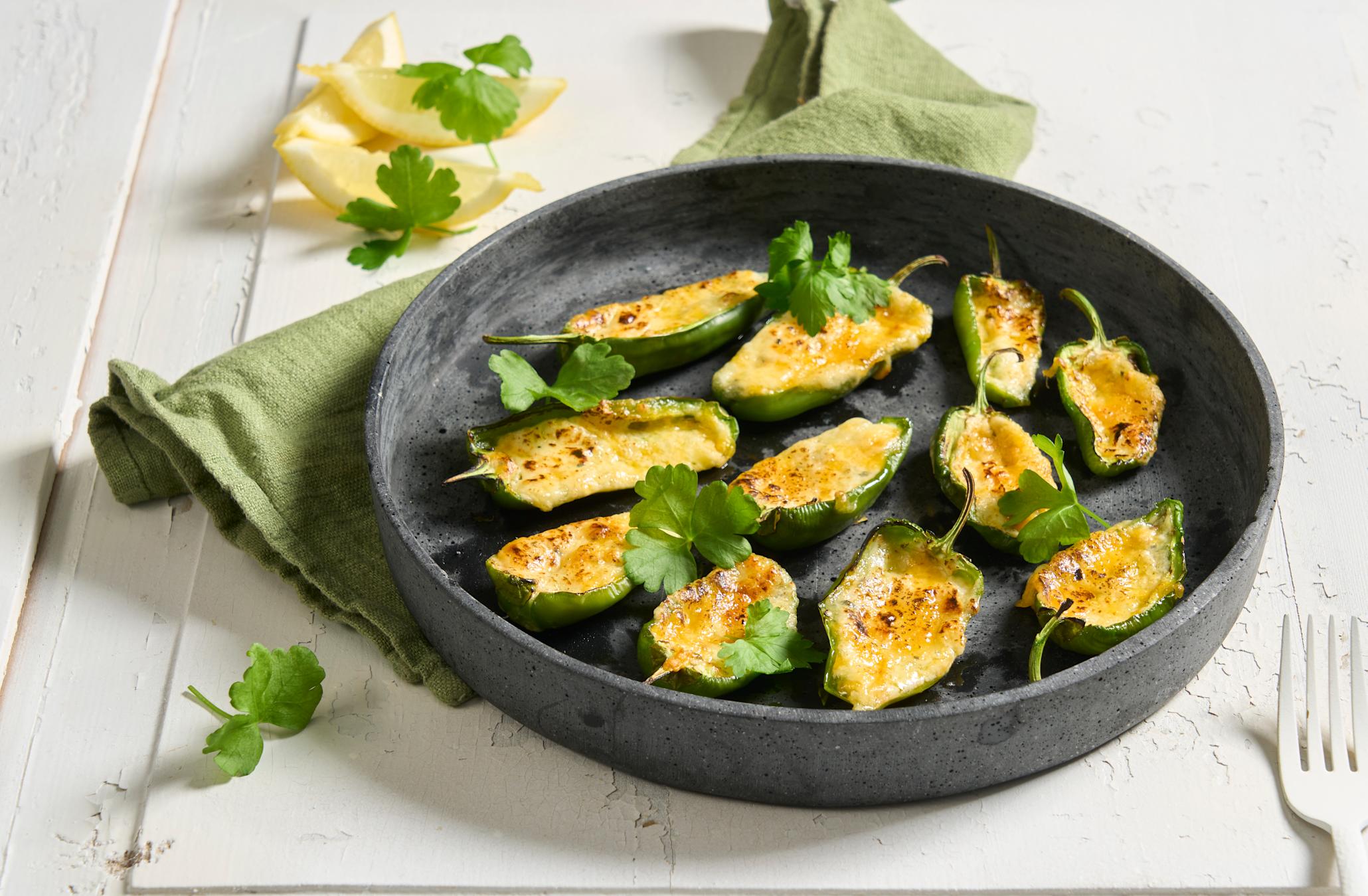 Fylt padron på grillen med blåmuggost og cheddar servert på mørkegrått fat med bladpersille strødd over. Sitronbåter i bakgrunnen.