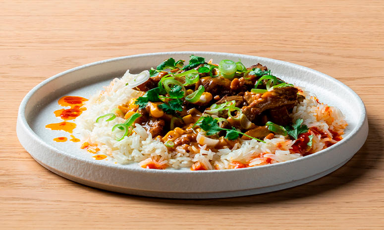 Biff satay med ris og grønnsaker servert på en hvit tallerken med høy kant på tallerkenen