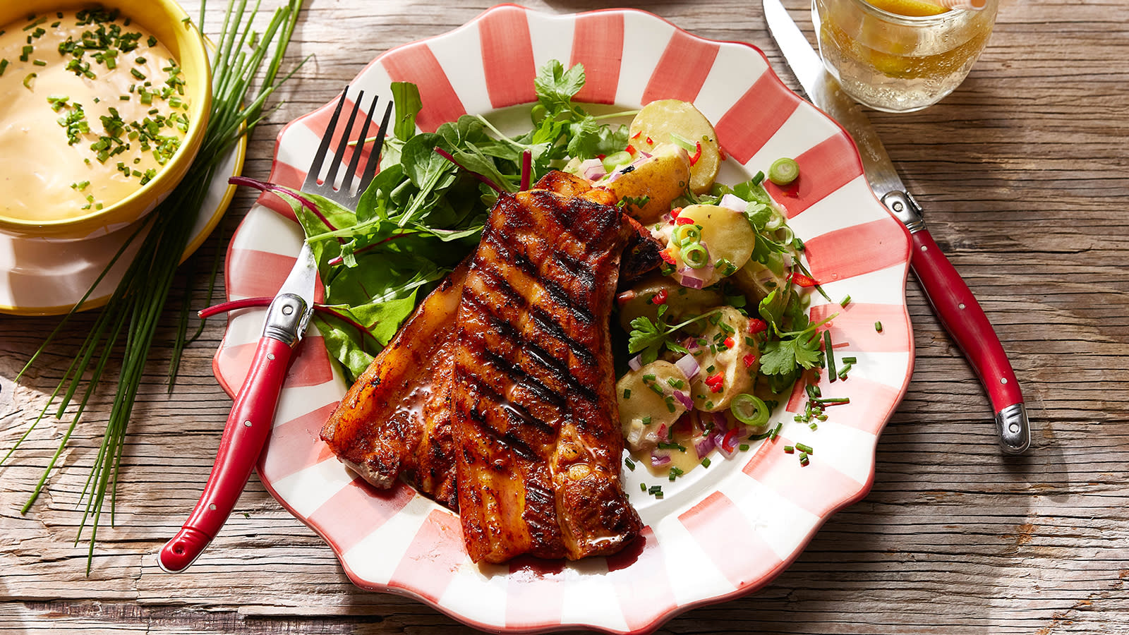 Grillribbe med syrlig potetsalat servert på rødstripet asjett med chili bearnaise ved siden av.