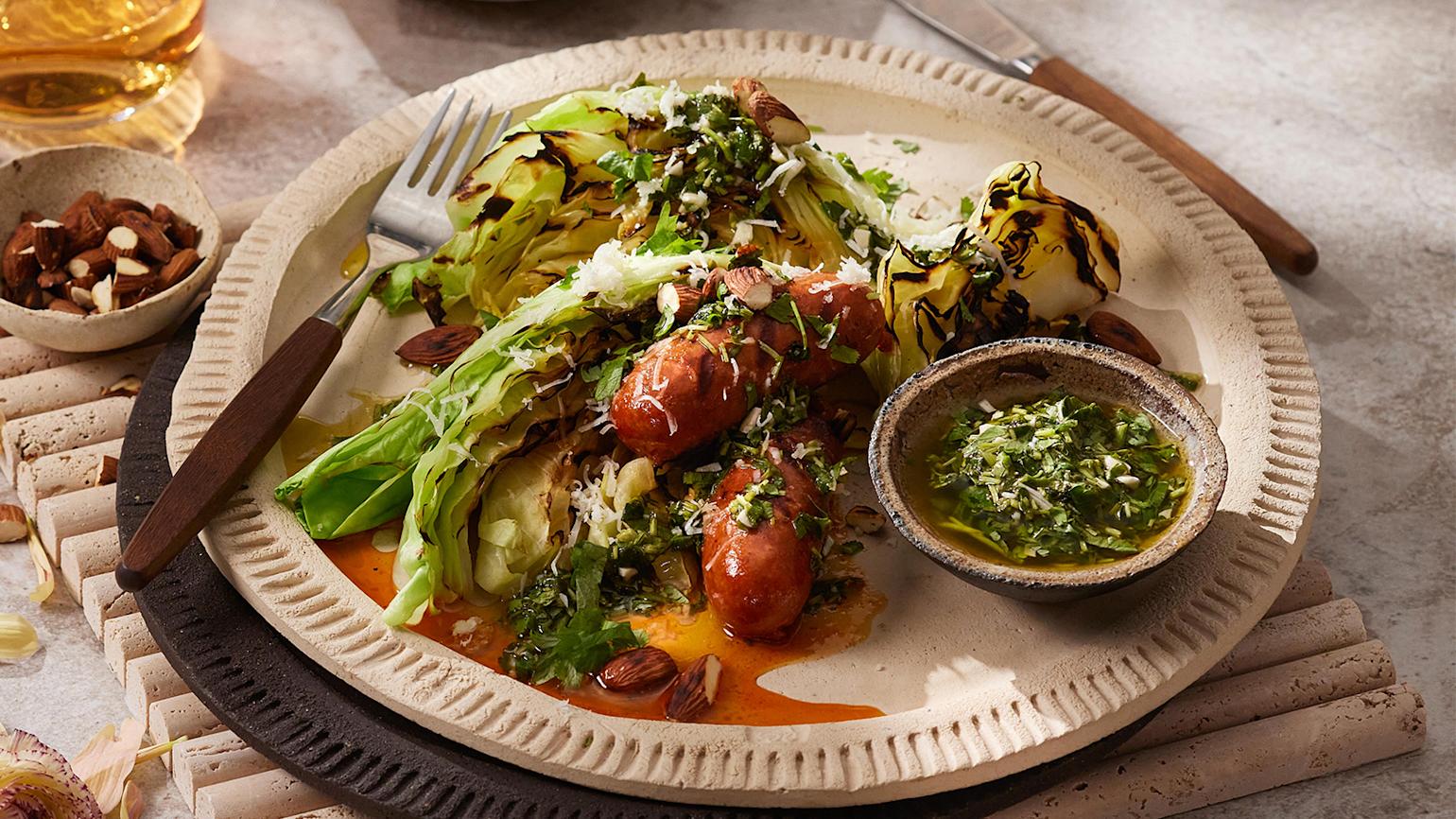 BBQ chorizo med grillet nykål og chimichurri servert på lys tallerken med en skål hakkede mandler ved siden av.