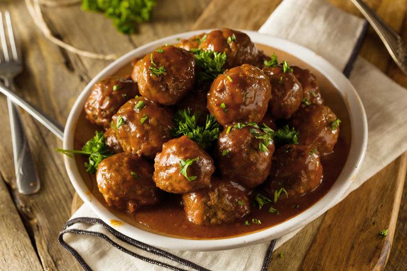 Hjemmelagde kjøttboller i brun saus, servert på hvitt rundt fat, og rustikk trebakgrunn. Dryss med fersk persille på toppen.