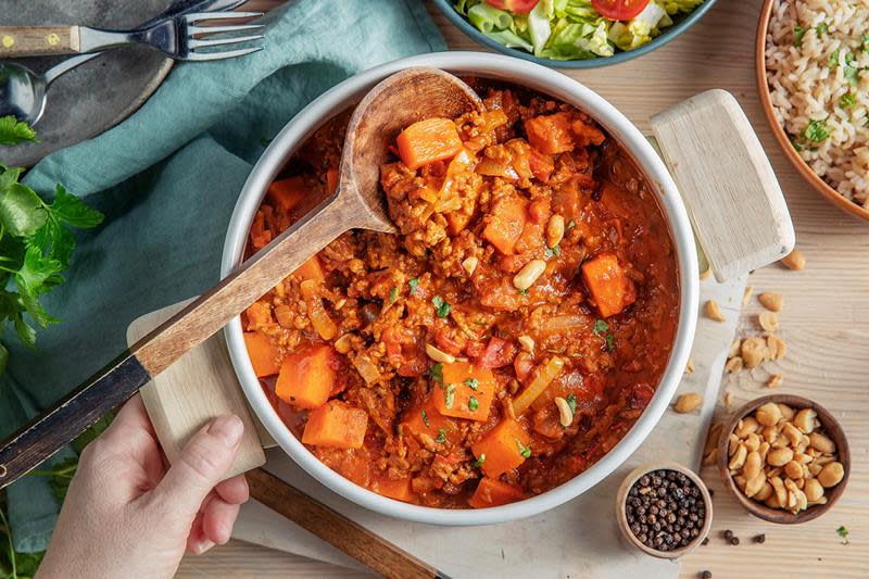 Fargerik kjøttdeiggryte med grønnsaker og peanøtter, servert i en lys kjele, med salat og ris på siden.