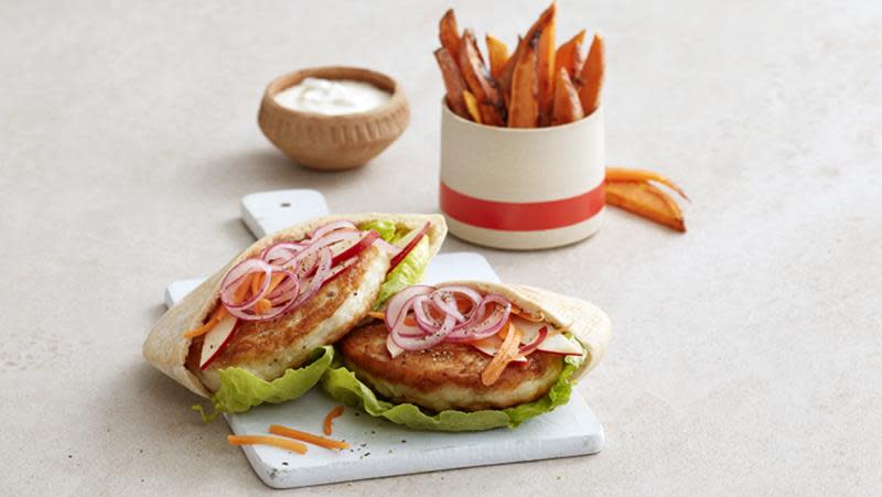Fiskeburger i pitabrød med salat, rødløk og gulrot på hvit trefjøl. Søtpotetfries og creme fraiche dressing på siden.