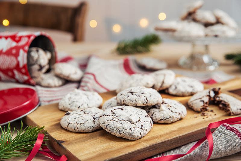 Flere av julekaken vepsebol med sjokolade og mandler, servert på rustikk trefjøl. Julepyntet bord, rød kakeboks og rødt julebånd i bakgrunnen.