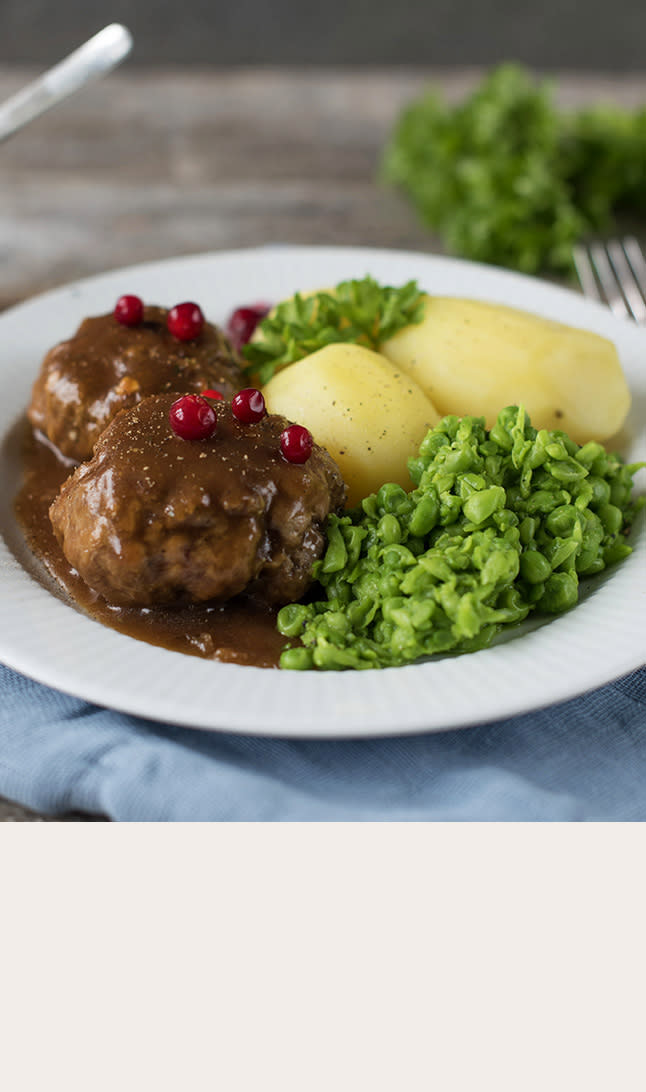 Mors kjøttkaker på hvit tallerken med kokt potet og ertestuing, servert på rustikk trebord med blå serviett.