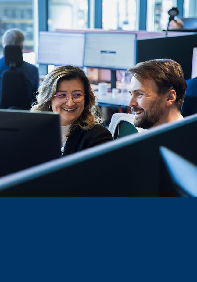 to kollegaer sitter og smiler foran en PC skjerm