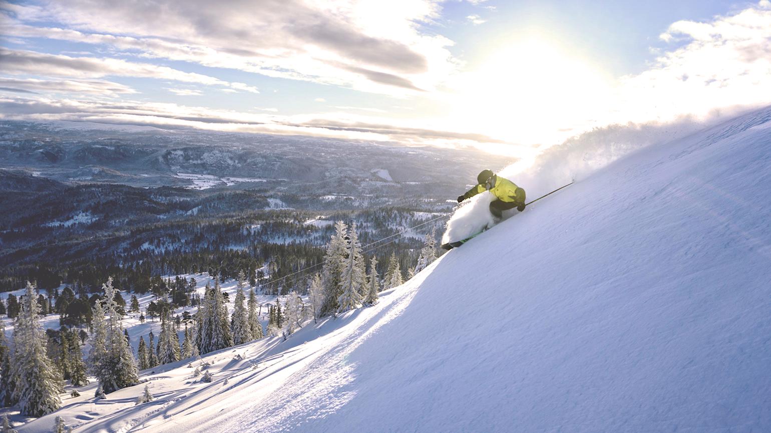 Mann står på slalom nedover bakke i nysnø
