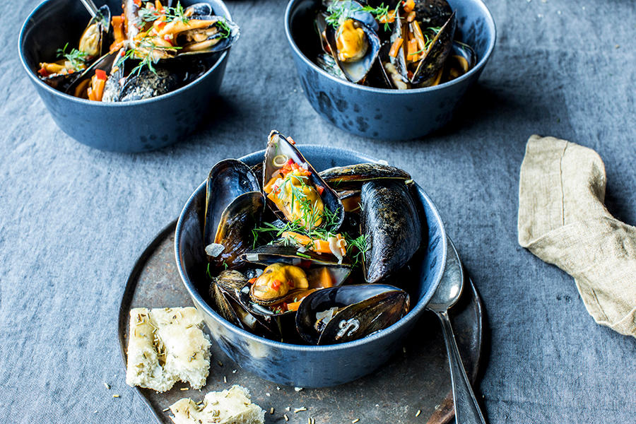 Dampede blåskjell med eplemost, chili og sitrongress servert i mørkeblå skåler med frisk dill over, og focaccia på siden.