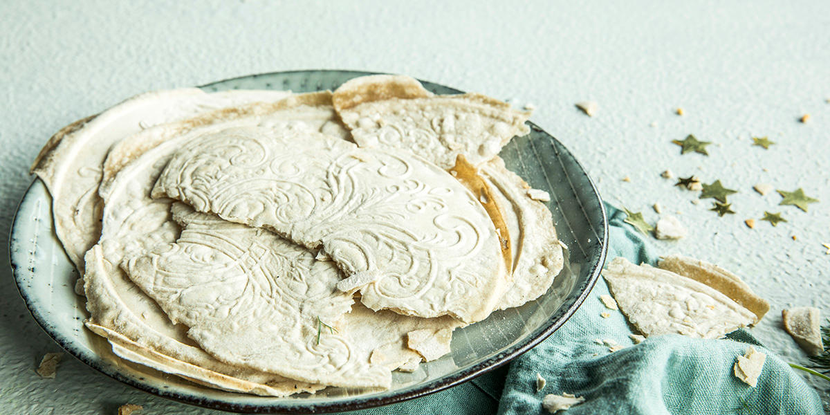 Hjemmelaget flatbrød med julemønster delt i mindre biter og servert på grønn asjett på linserviett. Små gullstjerner strødd ved siden av asjetten.