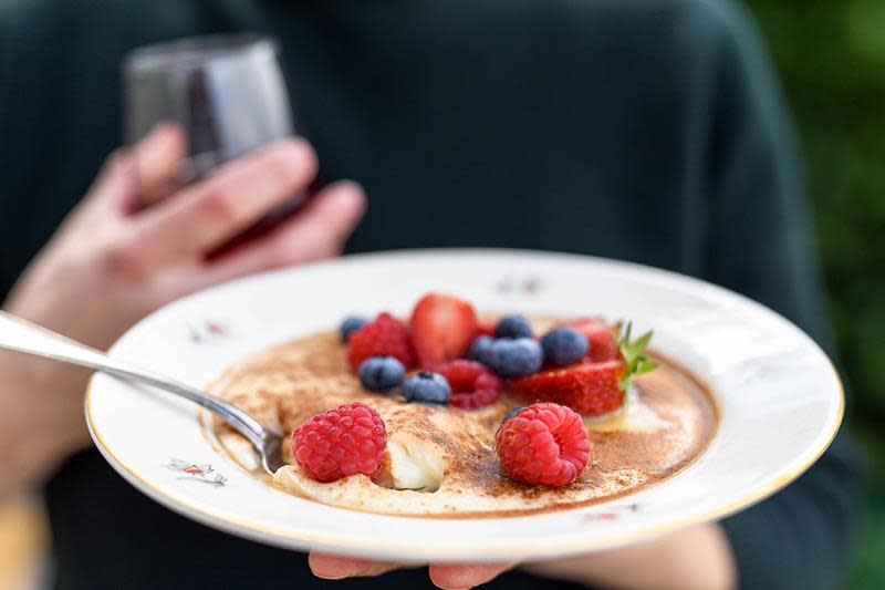 En hånd holder frem en tallerken med fløyelsgrøt, toppet med kanel, sukker, ferske bringebær, blåbær og jordbær.
