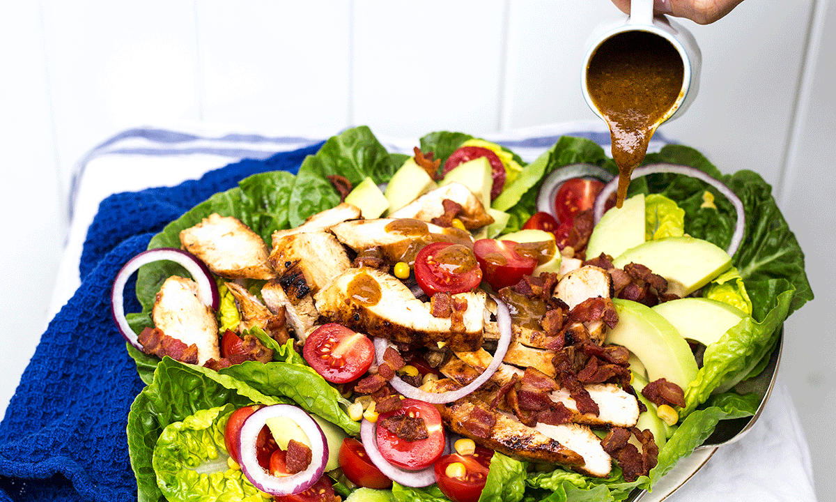 Kyllingsalat med bacon og avokado, tomat og rødløk. Servert på avlangt fat, med dressing helt over.