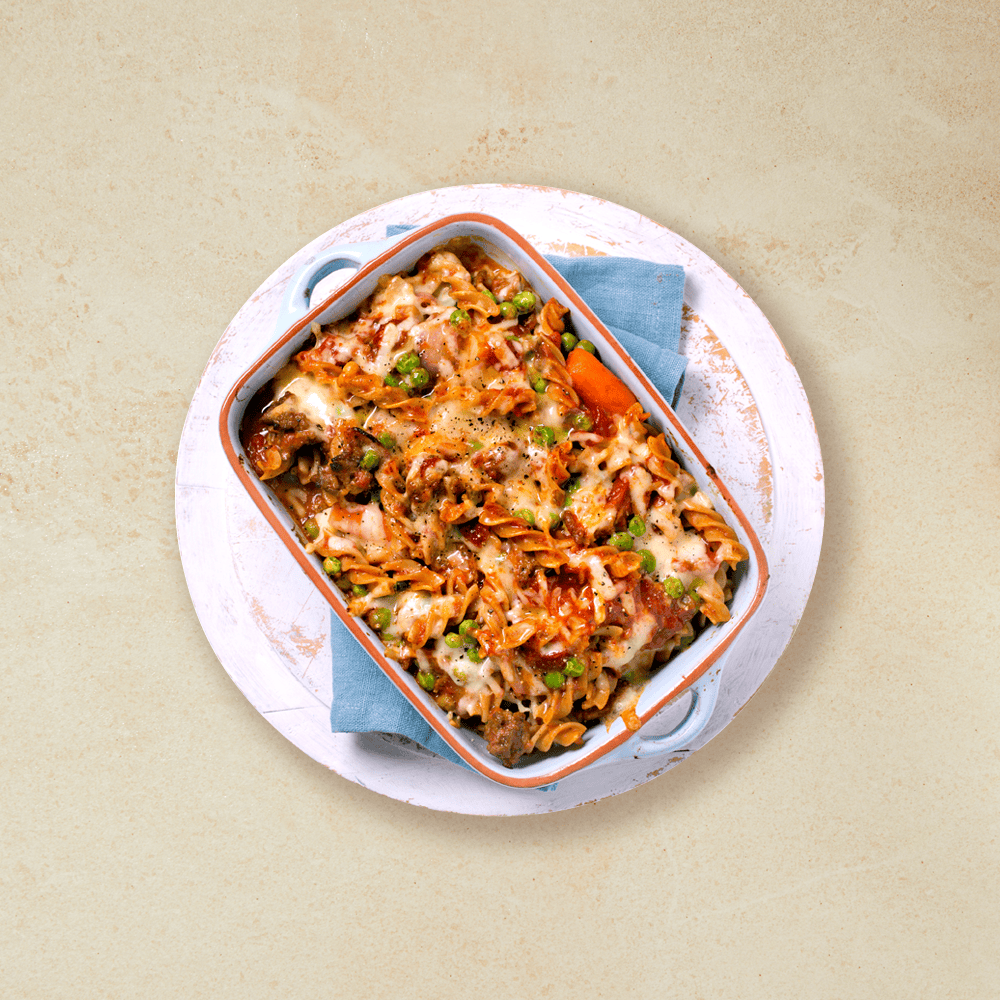 Pastagrateng i en lys blå ildfast form som står på et blått håndkle