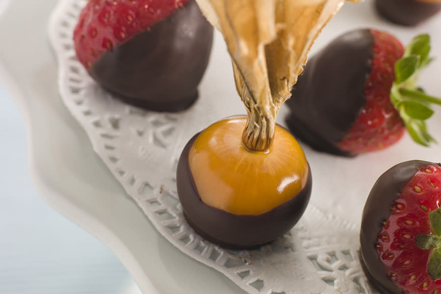 Physalis og jordbær dyppet i sjokolade, og servert på hvitt fat med hvit pynteduk.