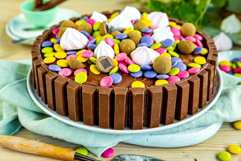 Kvikklunsjkake med sjokoladekrem pyntet med Kvikklunsj rundt kanten, Non Stop, marengs og lakriskuler. Servert på hvitt fat, med turkis linserviett under.