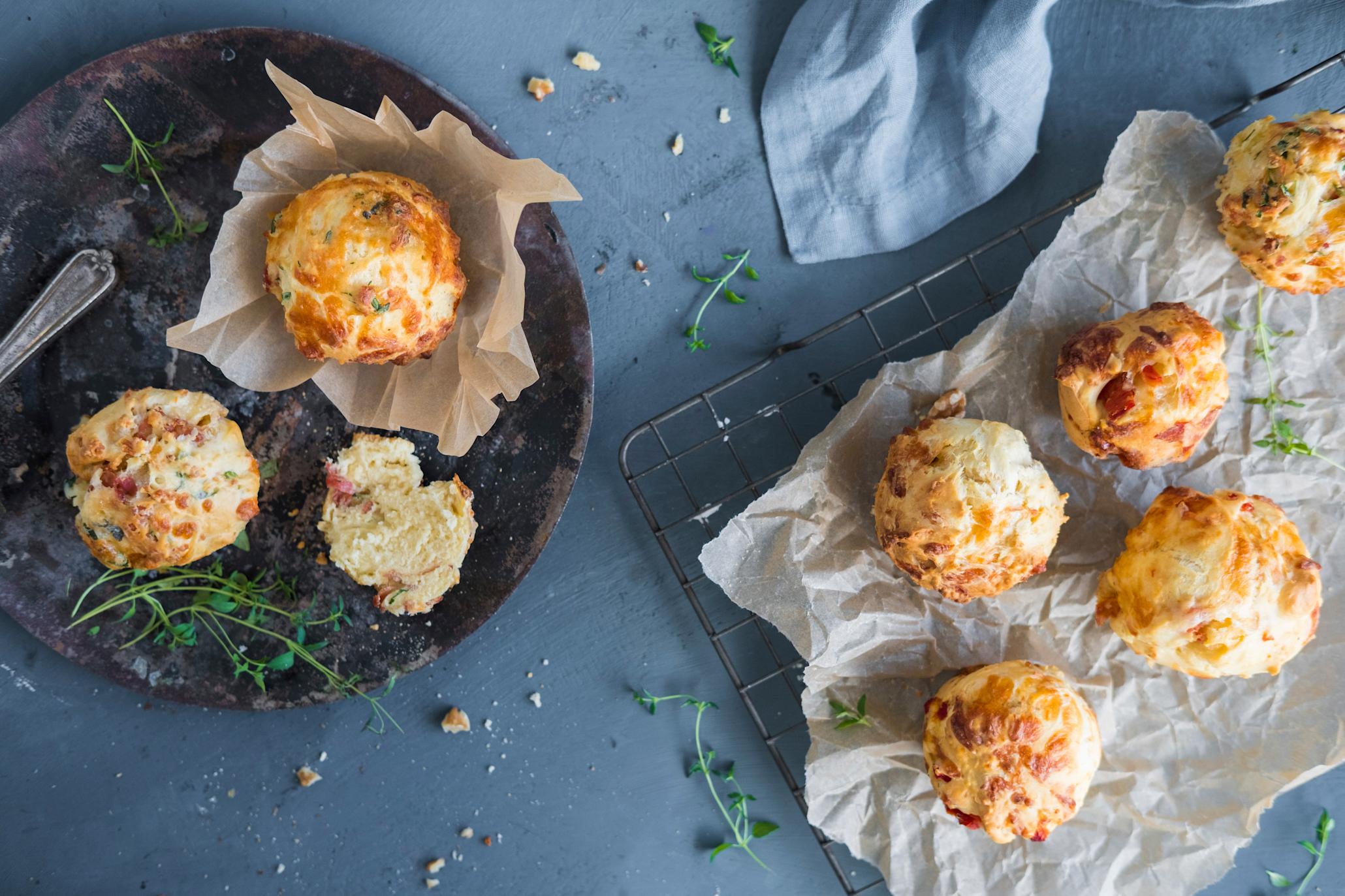 Matmuffins med tre deilige fyll av ost, skinke og nøtter servert på mørk rund trefjøl og firkantet metallrist med krøllet bakepapir. Friske kvister timian strødd omkring.