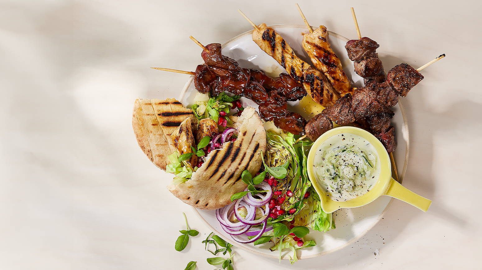 Grillspyd-miks med nykål, tzatziki og pitabrød. Servert på hvit tallerken.