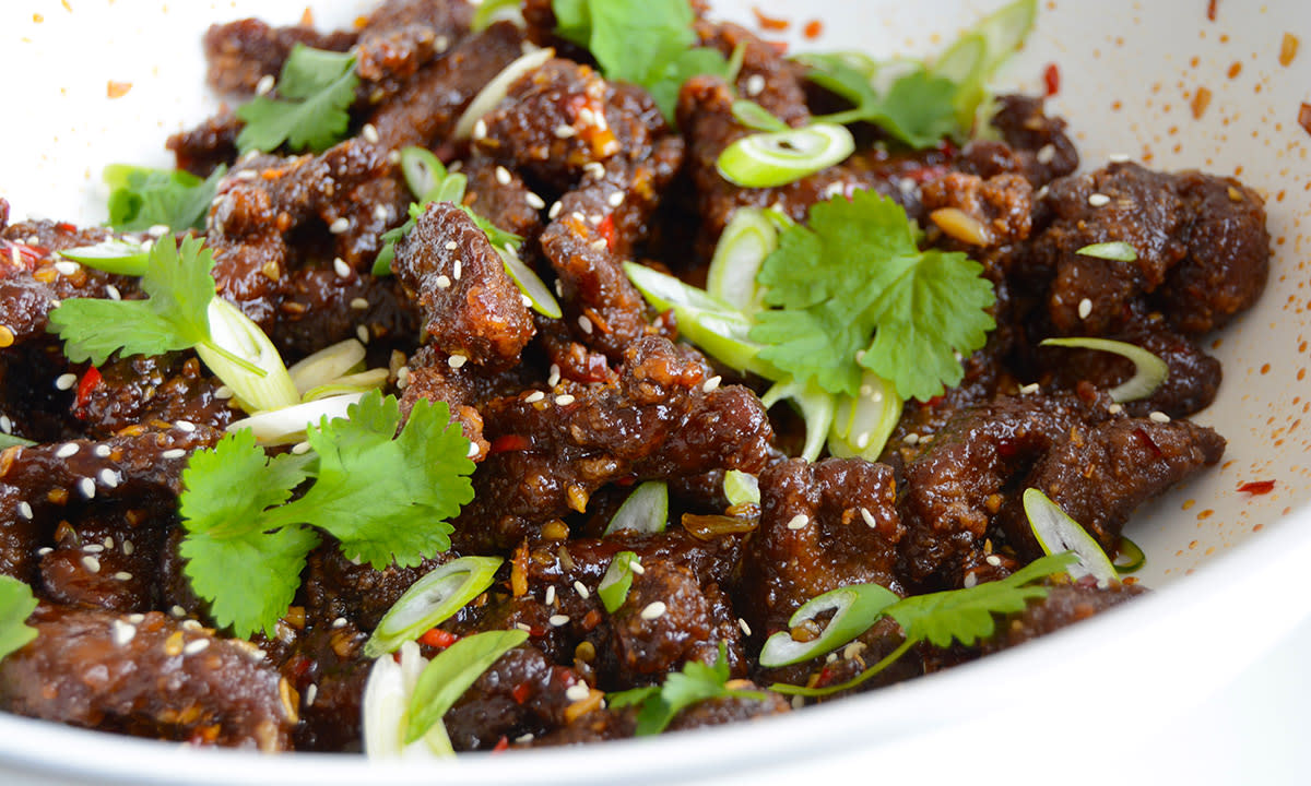 Kinesisk chilibiff med vårløk i skiver, og frisk koriander, servert på hvit tallerken.