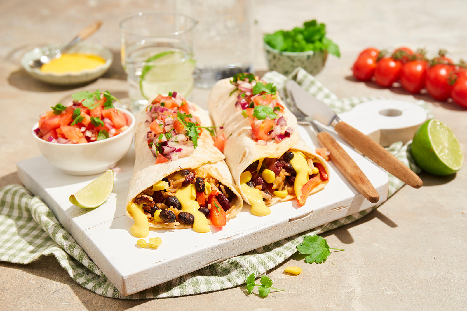 Vegetar burrito med krydrede bønner og Kavli Cheddar Dipp servert på hvit trefjøl med hjemmelaget tomatsalsa på toppen. Liten hvit skål med tomatsalsa ved siden av, og skål med cheddar dipp i bakgrunnen.