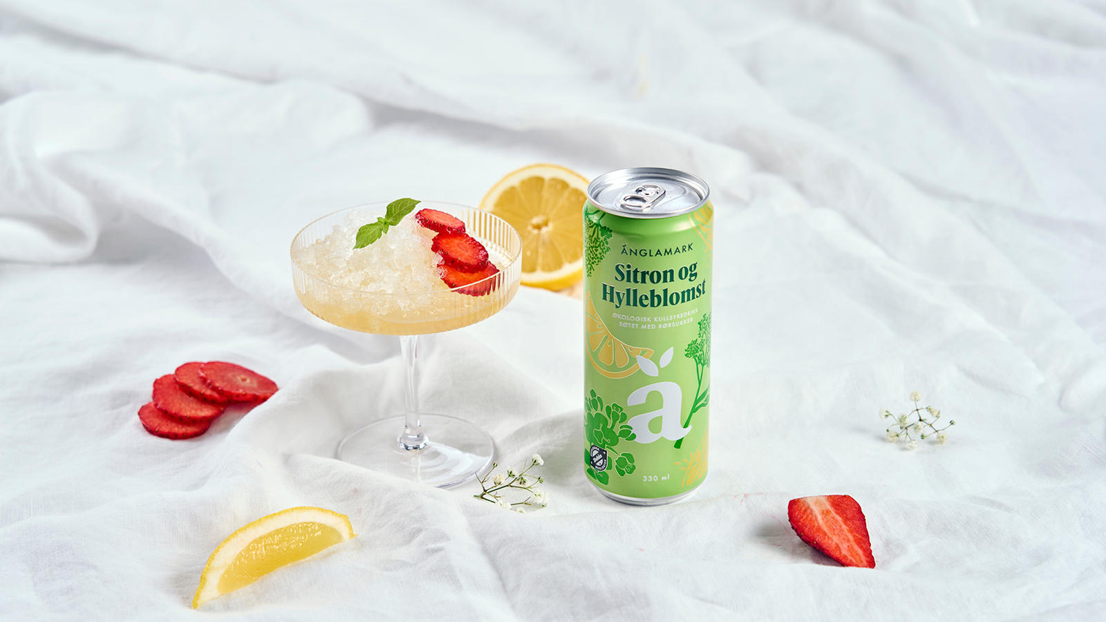 Sitrongranité med hylleblomst servert i cavaglass ved siden av en boks Änglamark Sitron og Hylleblomst. Hylleblomst, friske jordbær og sitronskiver rundt.