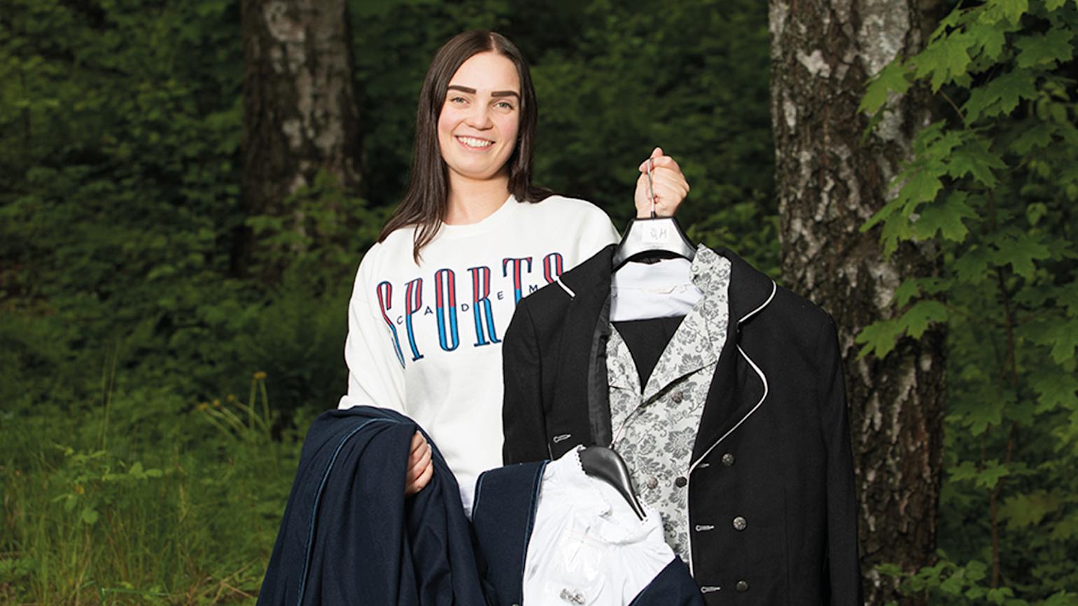 Dame står i skogen og smiler og viser frem budnader.