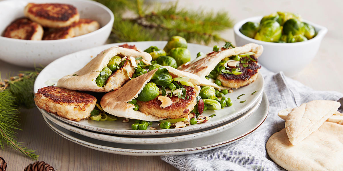 Vegisterkaker i pitabrød, servert med rosenkål og skivede mandler på lys tallerkenstabbel.